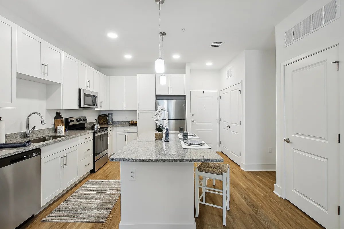 Modern kitchen with sleek white cabinetry, stainless steel appliances, and elegant countertop island with seating. - Lamplighter Legacy