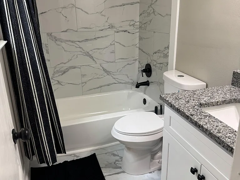 Updated full bath with marble-look tile surround, tub/shower combo, and vanity with granite-style countertop.