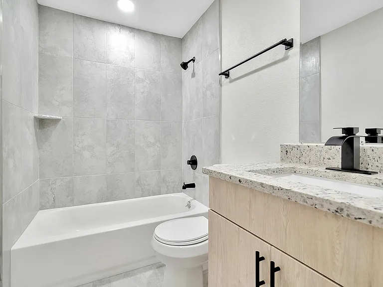 Elegant bathroom with modern fixtures, featuring a sleek granite countertop, spacious tub, and stylish matte black accents.