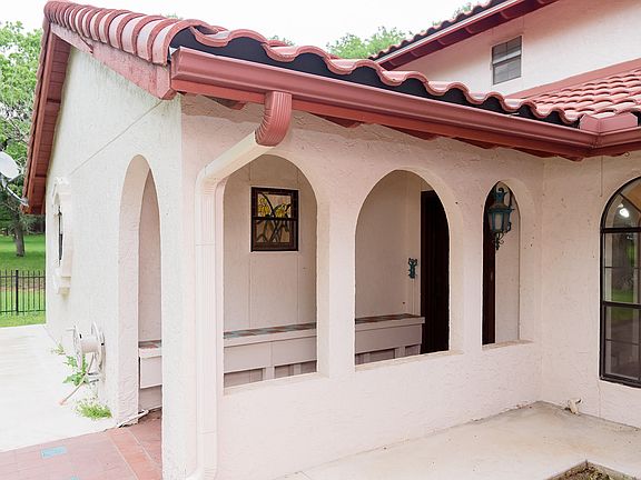 The front entry of this stunning stucco home with a tile roof is framed by elegant archways, offering a warm and inviting first impression with classic architectural charm.