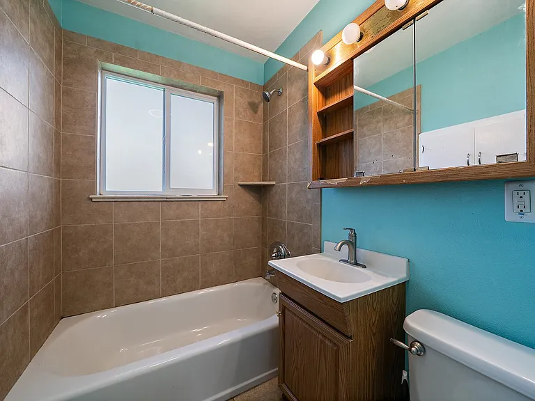Tiled bathroom with medicine cabinet and shelves. Large frosted window to backyard.