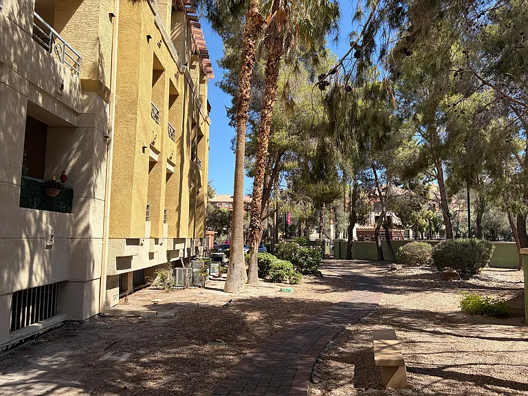 Exterior view of the private balcony and surrounding landscaped grounds, with mature trees providing shade to the balcony area all day long and enhancing the peaceful setting just outside the unit.
