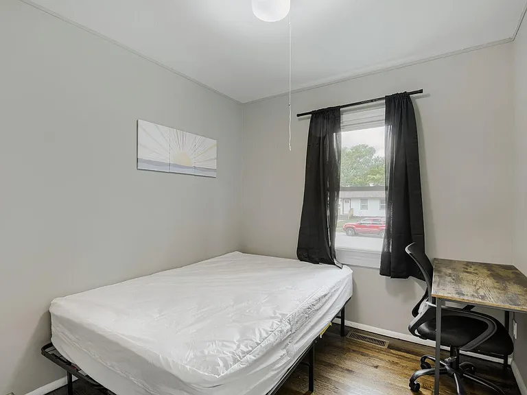 Furnished bedroom with a bed, work desk, and window with curtains, offering a functional layout for rest and study.