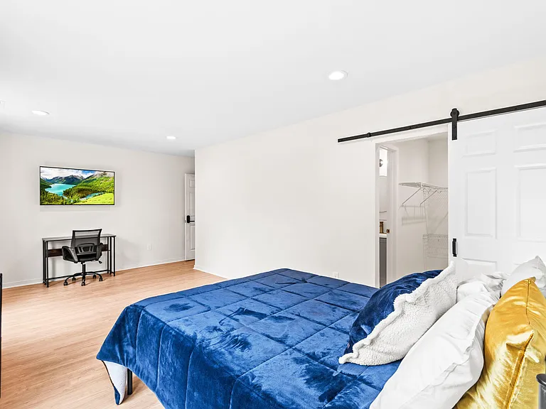 Spacious bedroom with wood-look floors, a dedicated desk area, and a large closet with sliding barn-style door.