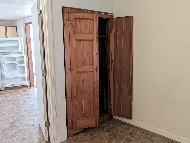 View of the 3rd bedroom showing door into the kitchen and the cabinet that forms the closet for this room. The door into the room is on the photographer's right, and the back entrance to the house is behind and to the left of the photographer.
