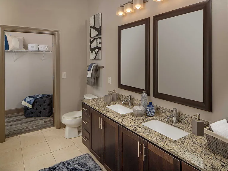 Bathroom with double sinks, granite counters, and walk-in closet