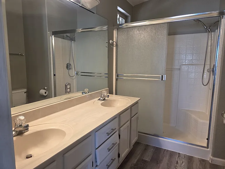 Master bath with double sinks and shower with two seats, glass doors and a handheld shower.