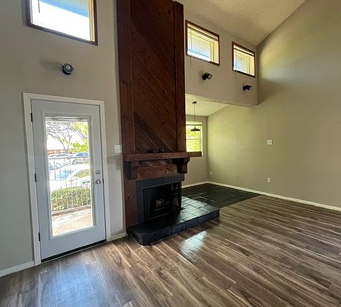 Another view of the ground floor, with brightly lit spaces, laminate flooring, large windows, a wood-burning fireplace, and a metal-glass door (with mini blinds) leading to the outdoor terrace.