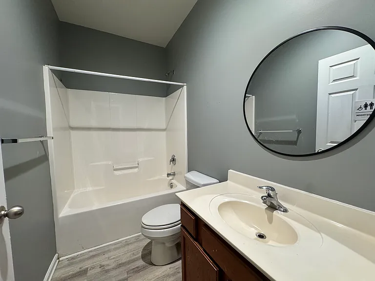 A clean, modern bathroom with a round mirror, vanity, and tub/shower combo. The second bathroom is well-maintained with bright lighting.