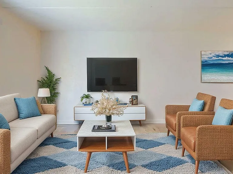 Inviting living room with stylish wicker furniture, elegant TV setup, and coastal artwork, perfect for relaxation and entertainment.