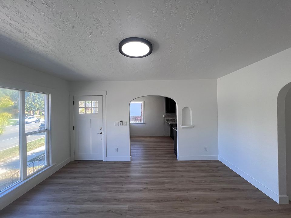 The large living room features oversized windows offering views of 25th Street and Ben Lomond Mountain. The open layout flows seamlessly into the kitchen. The room has been updated with new flooring and freshly painted white walls.