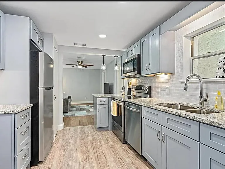 Galley kitchen with ample cabinetry, stone-look counters, stainless appliances, and double sink under the window.