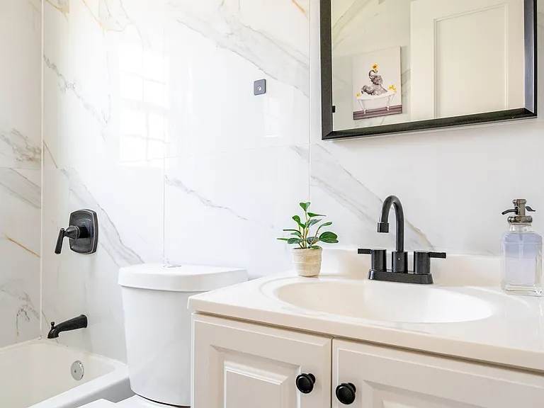 Updated full bath with tub/shower, marble-look tile surround, and vanity with storage and matte black fixtures.