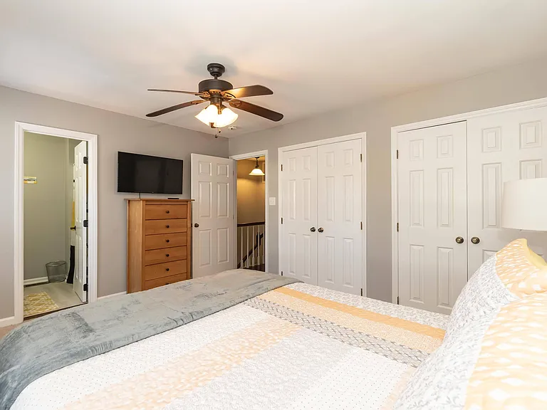 Spacious bedroom with ceiling fan, wall-mounted TV, and double-door closet storage for easy everyday organization.