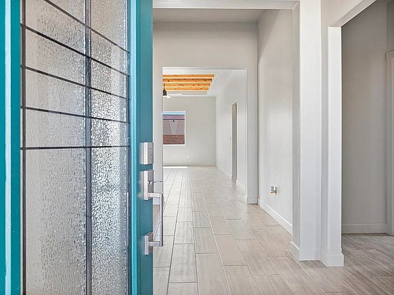 Open blue front door revealing a modern, bright hallway with light-colored tile flooring, white wall