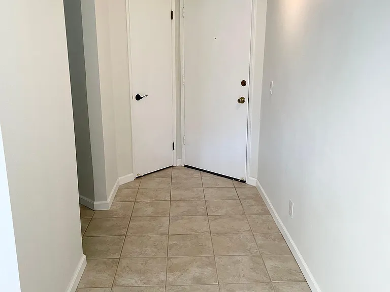 Entry hallway. Front door is on the right. Adjacent door leads to the bathroom area. Opening on the left wall leads to bedroom.