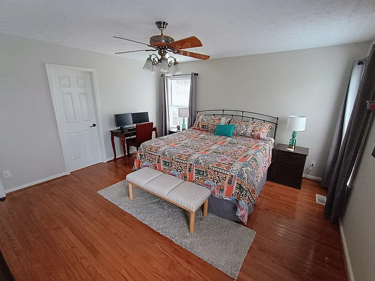 The primary bedroom features a workstation with a desk, chair, keyboard, and two monitors, along with a king size bed, a bench for added comfort, plus a small Smart TV.