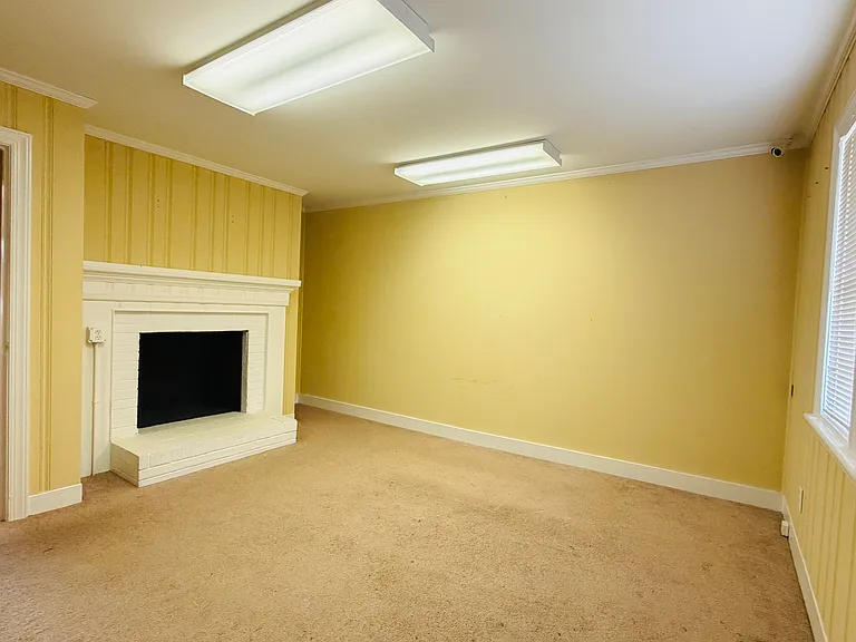 Spacious flexible room with decorative fireplace, bright neutral walls and ample overhead lighting.