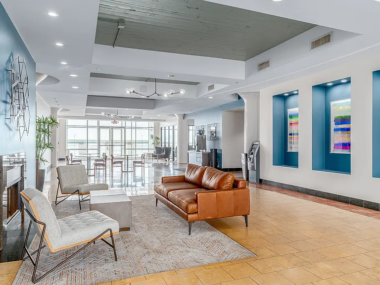 Elegant apartment lobby with modern decor, featuring a cozy seating area with a leather sofa, vibrant artwork, and expansive windows offering Lake Erie views