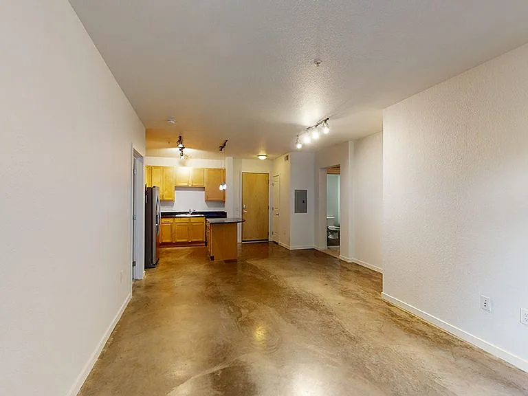 Apartment kitchen with stainless steel appliances, dining and living room with polished concrete flooring.