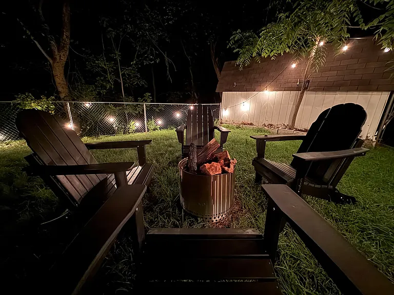 Backyard firepit with four Adirondack chairs and string lights _ fully fenced yard with private forest behind, on a quiet residential street