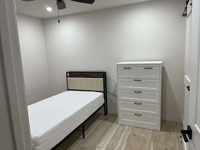 Primary bedroom furnished with TwinXL bed, tall dresser, desk, and chair.
