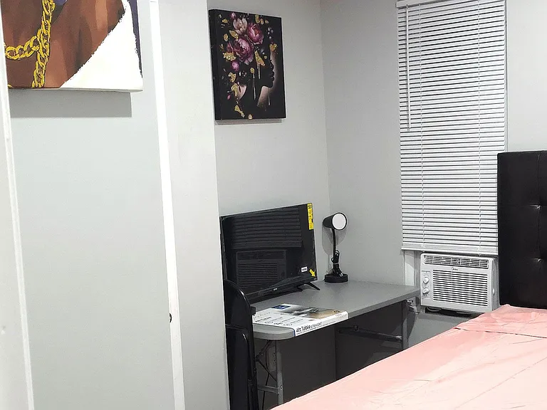 Furnished bedroom with a work desk setup, upholstered bed, and window A/C for added comfort and convenience.