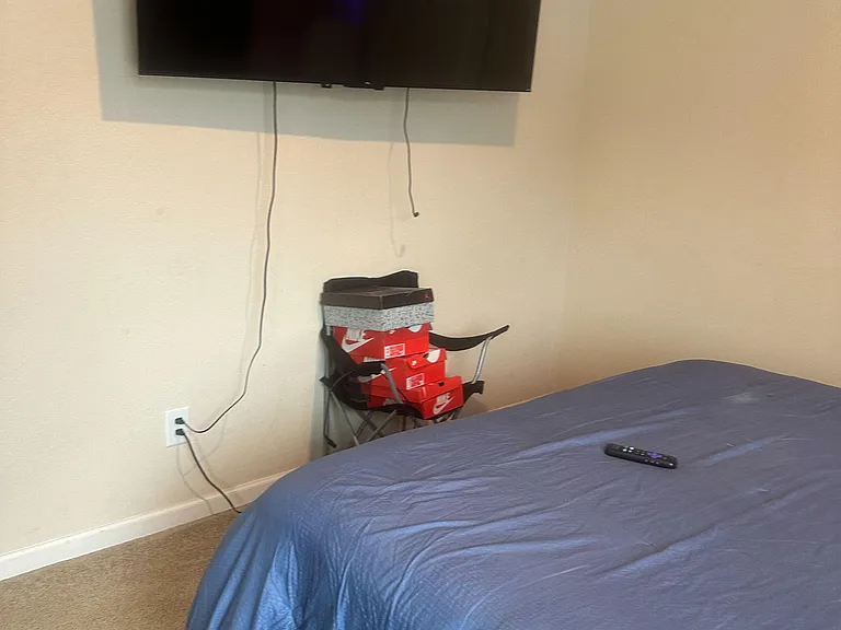 Carpeted bedroom with a comfortable sleeping area and wall-mounted TV, offering a simple setup for relaxing at home.