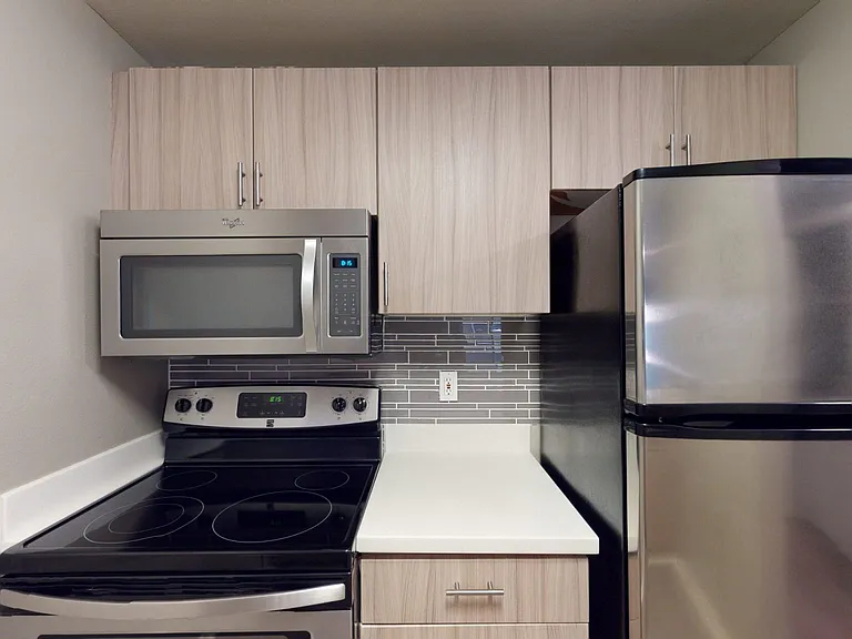 Apartment kitchen with stainless steel appliances, quartz countertops and wood-style flooring.