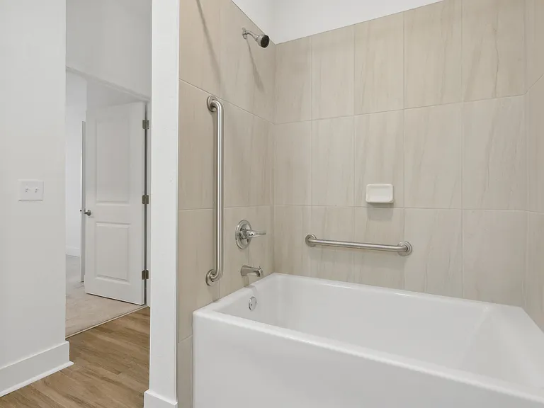 Elegant bathroom with a sleek, modern bathtub, neutral-toned tiles, and convenient safety rails.