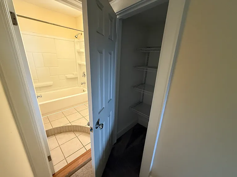 An upstairs closet with shelving is located adjacent to the bathroom.