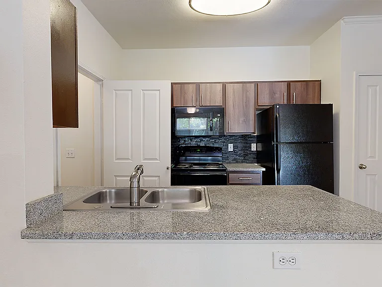 Apartment kitchen with granite countertops and wood-style flooring.