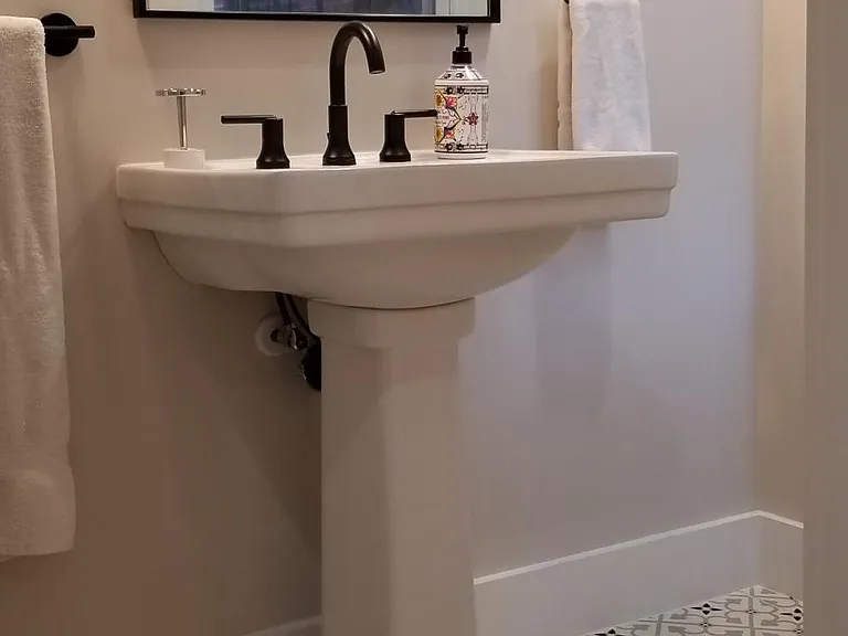 Pedestal sink and mirror reflecting window across from sink.