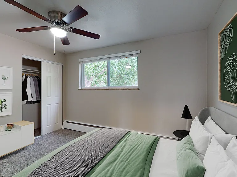 Inviting bedroom with a modern ceiling fan, large window, stylish wall art, and organized closet space with lush tree view.