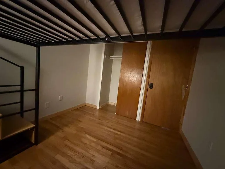 Bedroom with wood-look flooring and an open closet area, offering flexible space for sleeping and storage.