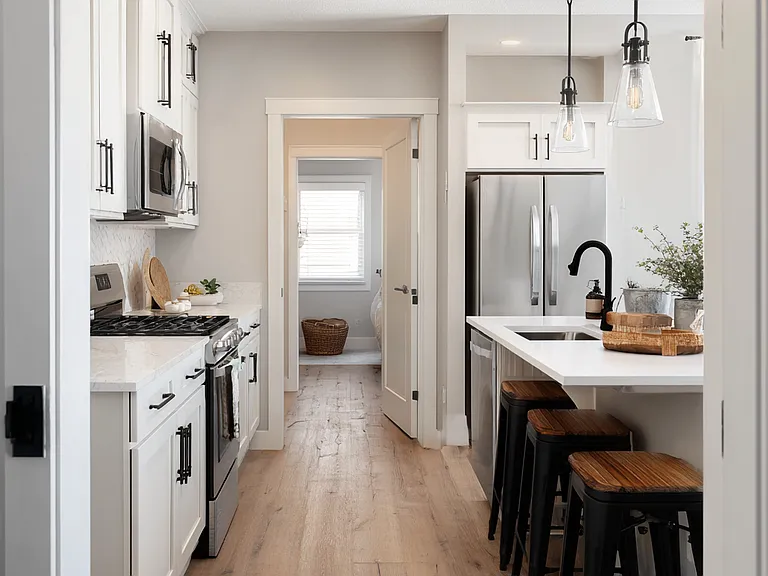 Modern farmhouse kitchen with white shaker cabinets, black hardware, stainless steel appliances, quartz countertops, and a 6-foot island with seating for four. Pendant lighting and LVP flooring throughout.