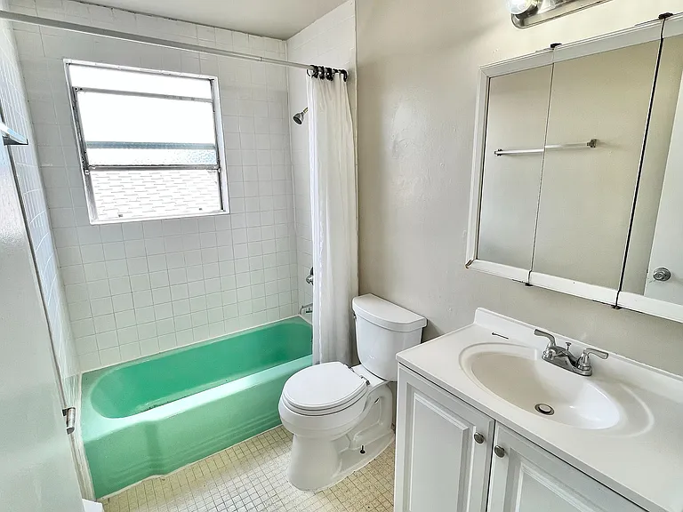 Bright and inviting bathroom with a retro green bathtub, elegant white tiles, and a modern vanity.