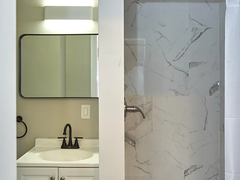 Updated bathroom with a single-sink vanity, framed mirror, and a shower/tub combo with marble-look tile surround.