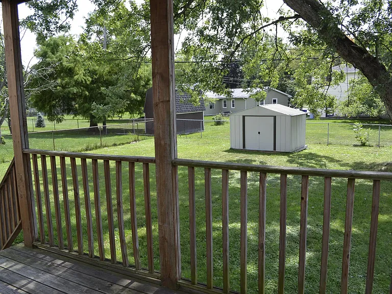 Lower deck with steps down to fenced back yard, shaded by mature tree.