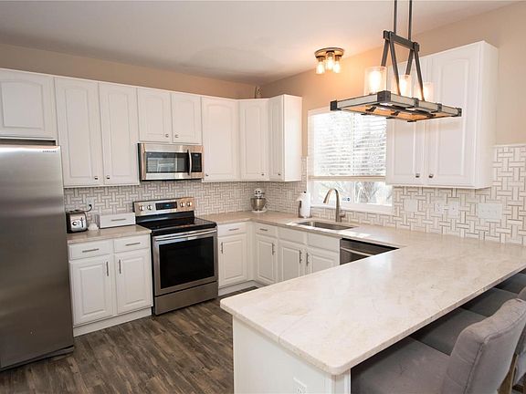 Kitchen w/ custom cabinet, quartz counter tops, wood floors, tile backsplash and stainless steel appliances.