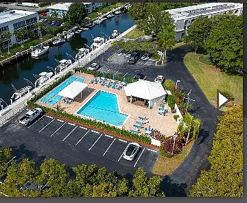 Aerial view of pool with cabana and a shaded lounge area right by one of the canals. This condo building is surrounded by water / canals