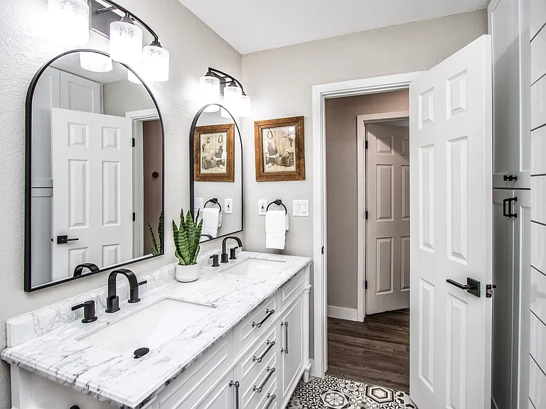 Modern double vanity at Casa Del Sol, Tempe rental home. Features a marble countertop, matte black faucets, arched mirrors, patterned floor tile, and bright vanity lighting. Stylish and functional bathroom setup for a top Tempe, AZ vacation stay.