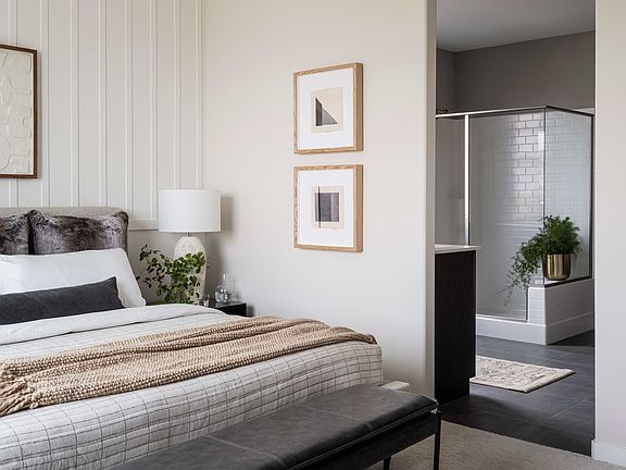 A cozy and modern bedroom with a large bed, framed artwork on the walls, and a sleek chandelier over