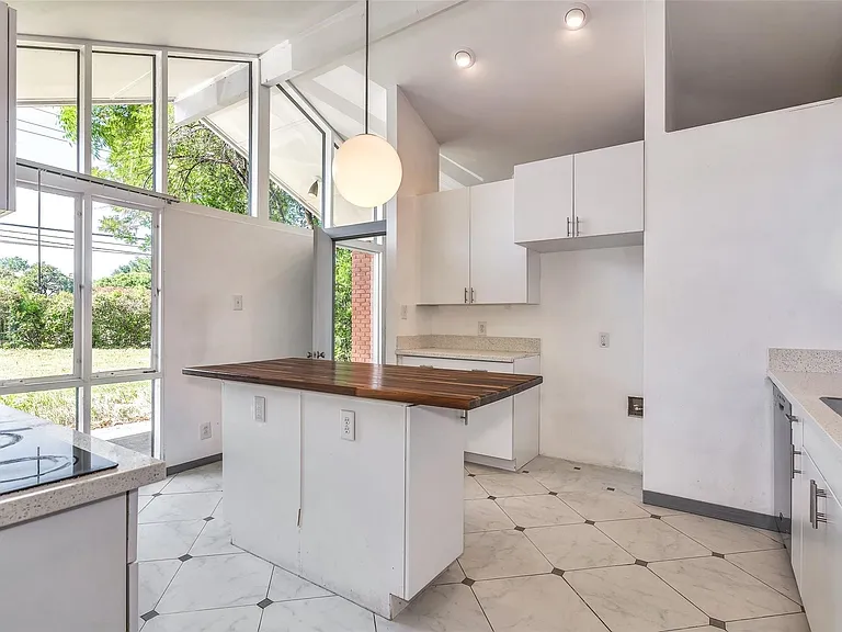 Kitchen featuring a central island with a wood-finish countertop, white cabinetry with silver-tone hardware, and light-toned countertops