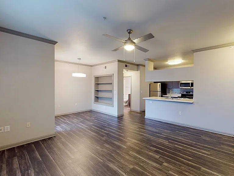 Apartment kitchen with stainless steel appliances, dining and living room with wood-style flooring.