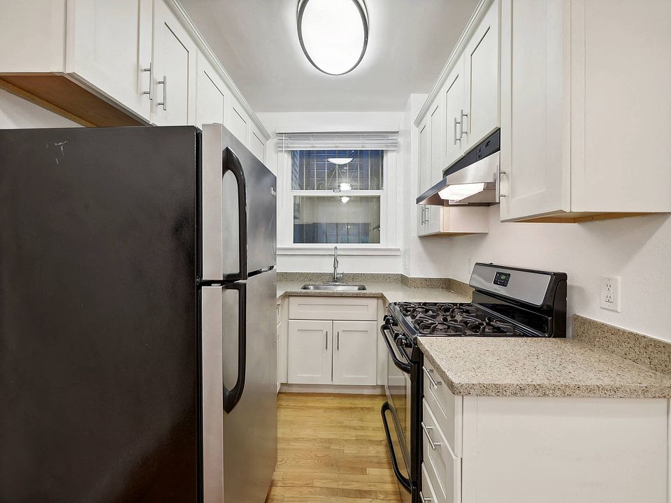 Kitchen with multiple cabinets, refrigerator, stove, range hood, and sink