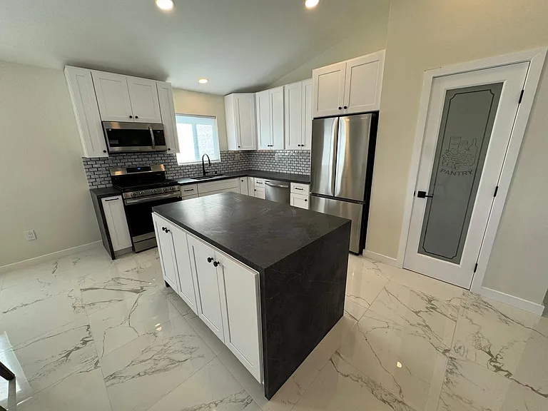 Kitchen with new SS appliances, quartz countertops, white shaker cabinets, workstation sink, island and under cabinet lighting.