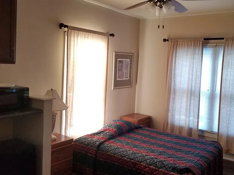 Private bedroom with a ceiling fan, two windows with curtains, and space for a full/queen bed and nightstands.