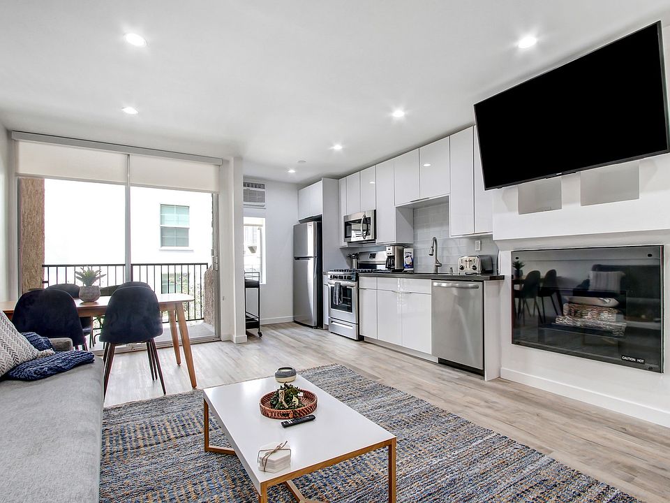Furnished 1 Bedroom Suite, living room with cozy fireplace, dining area on the left with private balcony, open kitchen