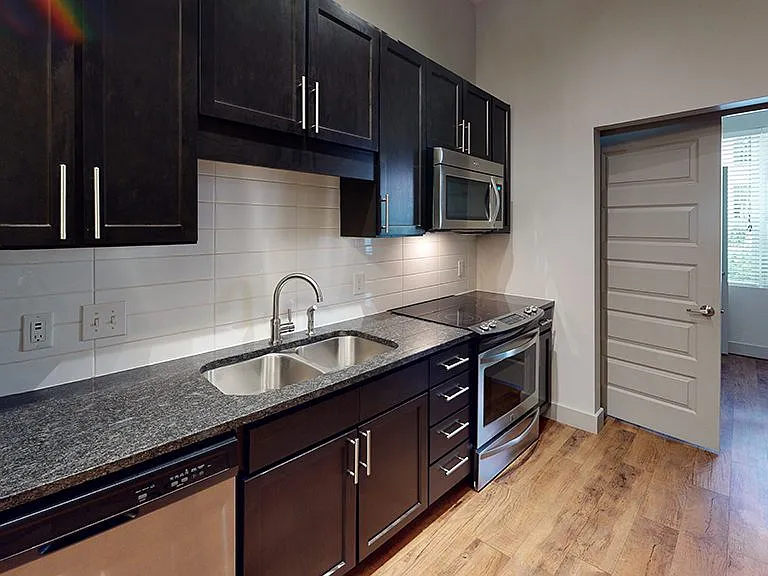Apartment kitchen with stainless steel appliances, granite countertops and wood-style flooring.